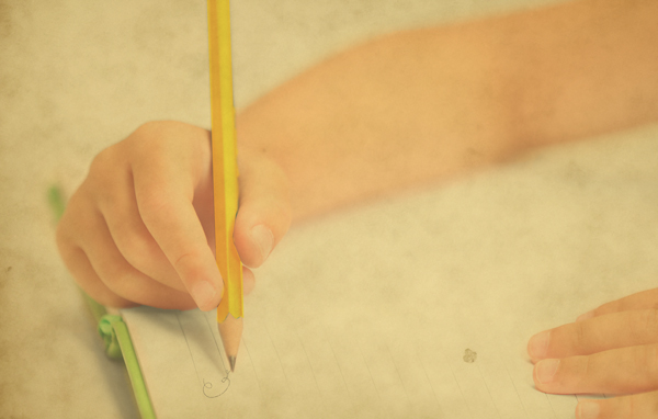 Photo of a young child holding a number 2 pencil writing a script letter 